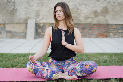 Woman practicing yoga while sitting on exercise mat over grass