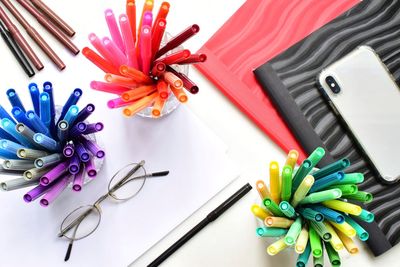 Close-up of multi colored pens with books and mobile phone on table