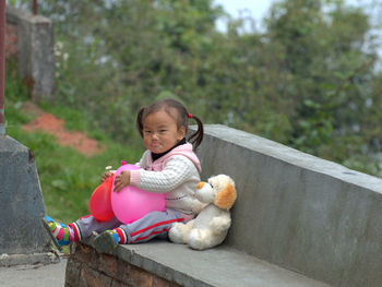 Portrait of cute baby girl with toys sitting on bench