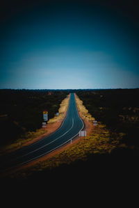 Country road leading towards city against blue sky