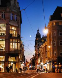 Illuminated street amidst buildings in city at dusk