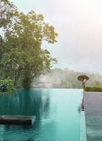 Scenic view of a woman with umbrella besides a infinitypool in the jungle during rain.