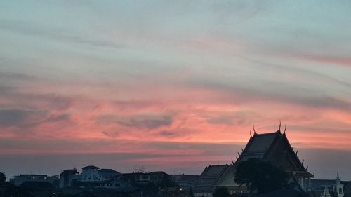 Silhouette city against dramatic sky during sunset