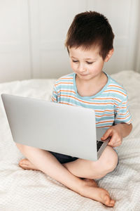 Teaching children at home using the internet. the schoolboy sits on the bed and watches the lesson