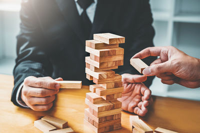 Midsection of businessmen stacking wooden blocks on table