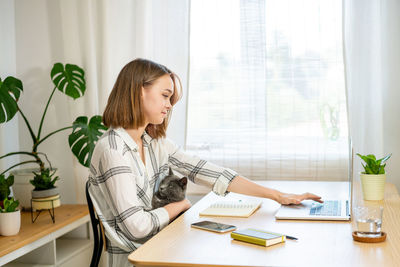 Young woman working on laptop at home. cozy home office workplace, remote work, e-learning concept.