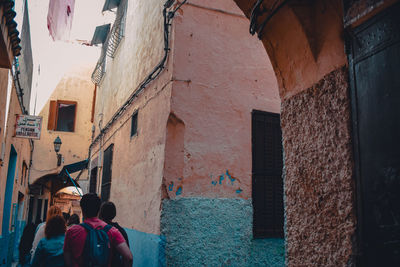 Rear view of people walking on alley amidst buildings in city