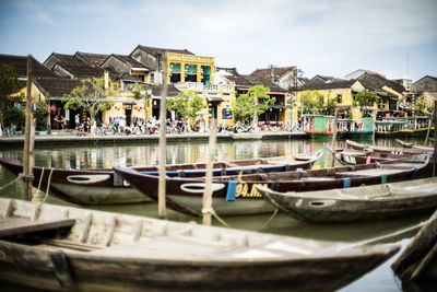 Boats moored in canal by buildings against sky