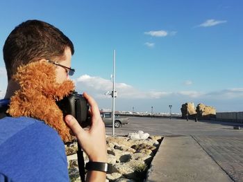 Man photographing with mobile phone against sky