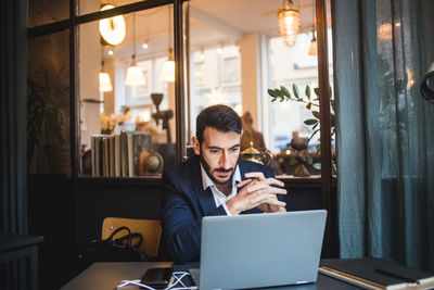 Confident businessman with hands clasped looking at laptop on desk in creative office