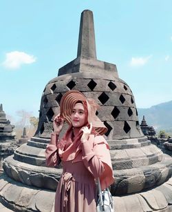 Young woman wearing hat standing against ancient sculpture