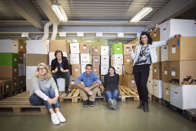 Portrait of smiling volunteers resting against cardboard boxes in workshop