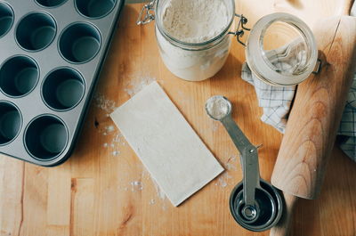 High angle view of flour with baking pan and measuring spoons on wooden table