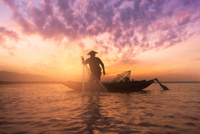 Fisherman casting net in lake against sky during sunset