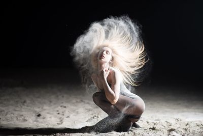 Seductive woman tossing sandy hair at desert during night