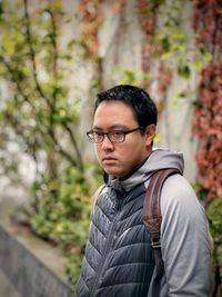 Portrait of young man wearing eyeglasses standing against trees