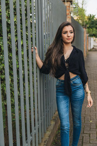 Thoughtful young woman standing by fence