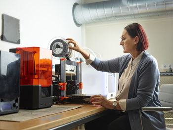 Engineer adjusting filament of 3d printer at workshop