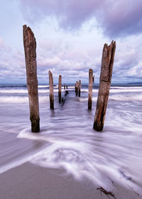 Wooden poles on a beach, the movement of the waves is shown in addition to a colorful evening sky