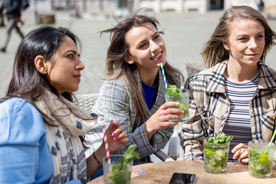 Smiling friends using smart phone while sitting at restaurant