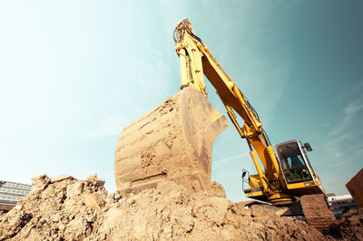 Low angle view of crane pulling mud at construction site against sky