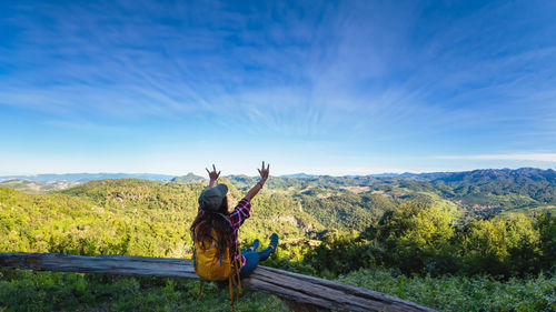 Rear view of woman sitting on mountain against sky