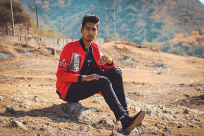 Handsome young man looking away while sitting on rock