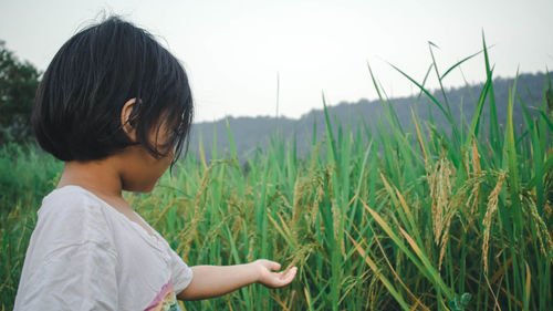 Side view of girl touching plants on field against sky