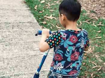 Rear view of boy riding push scooter on road