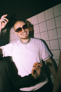 Smiling young man dancing against illuminated white wall