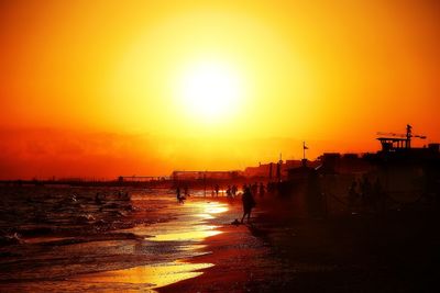 Silhouette people by sea against orange sky during sunset