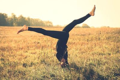 Side view of woman doing handstand on grassy field during sunny day