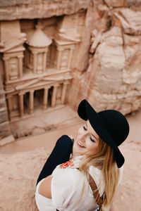 Young woman in hat sitting on rock formation