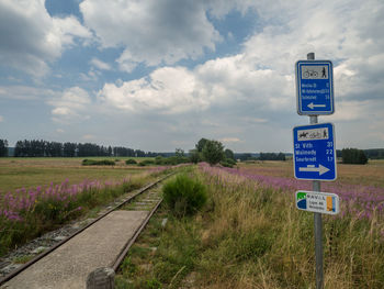 Road sign on field against sky