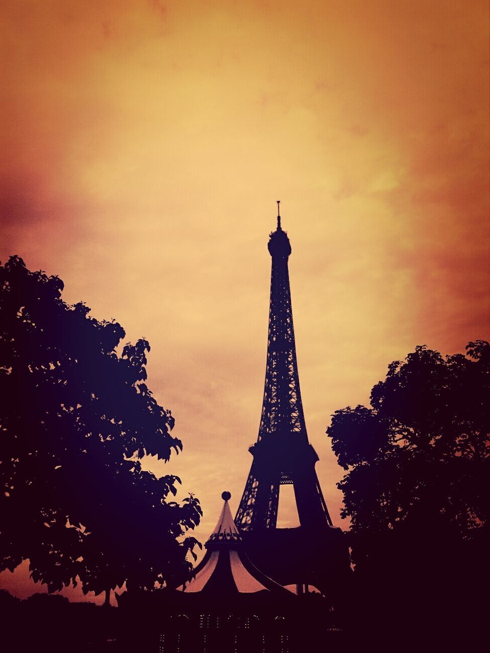 low angle view, built structure, architecture, tree, sky, sunset, silhouette, tower, eiffel tower, tall - high, dusk, travel destinations, famous place, metal, international landmark, tourism, outdoors, orange color, capital cities, cloud - sky