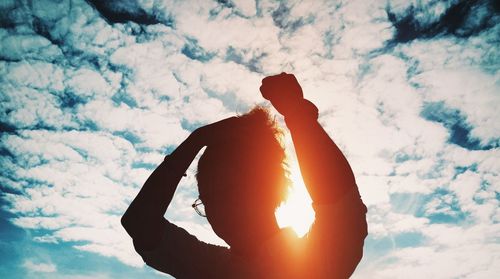 Silhouette man with arms raised standing against cloudy sky