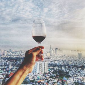 Cropped hand of man holding wineglass against cityscape