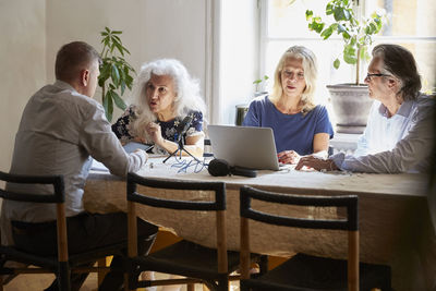 Senior friends discussing while vlogging on laptop at table