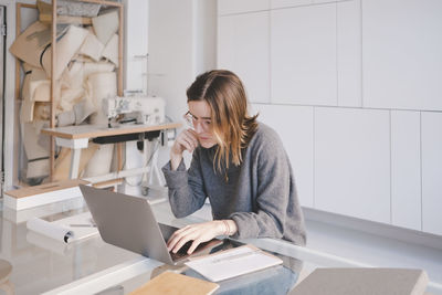 Young female fashion designer using laptop at desk in store