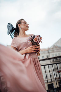 Low angle view of woman with arms outstretched standing against sky