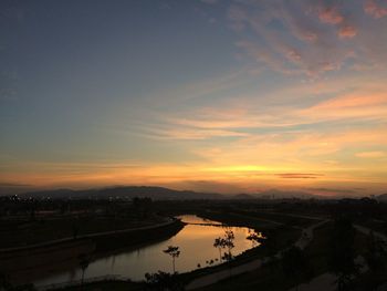 Silhouette city by river against sky at sunset