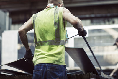 Rear view of blue collar worker using machinery while manufacturing sheet steel in industry