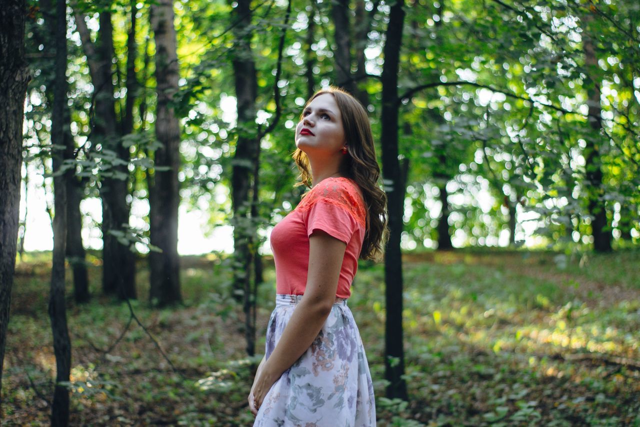 side view, tree, forest, young adult, standing, three quarter length, woodland, young women, leisure activity, tree trunk, lifestyles, person, solitude, focus on foreground, tranquil scene, tranquility, casual clothing, looking up, nature, long hair, scenics, beauty, non-urban scene, profile view, day, beauty in nature, outdoors, red