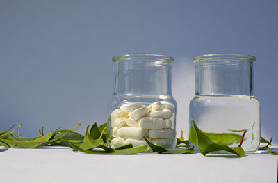 Glass jar with tablets of supplements, minerals, vitamins and a jar of clean water, green leaves. 
