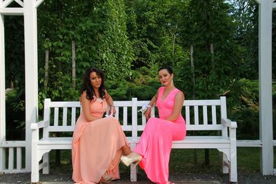 Portrait of beautiful women in wedding dresses sitting on bench in garden