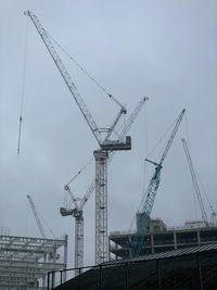 Low angle view of cranes at construction site against sky