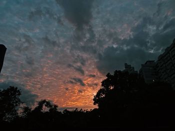 Low angle view of silhouette trees against dramatic sky
