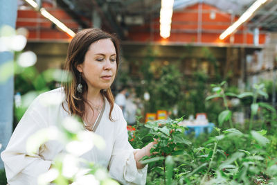 Brunette middle aged woman in white dress buys green potted house plants at garden store