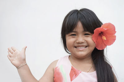 Portrait of smiling girl wearing hibiscus on hair against white background