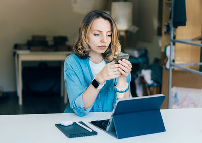 Mid adult woman using phone while sitting on table